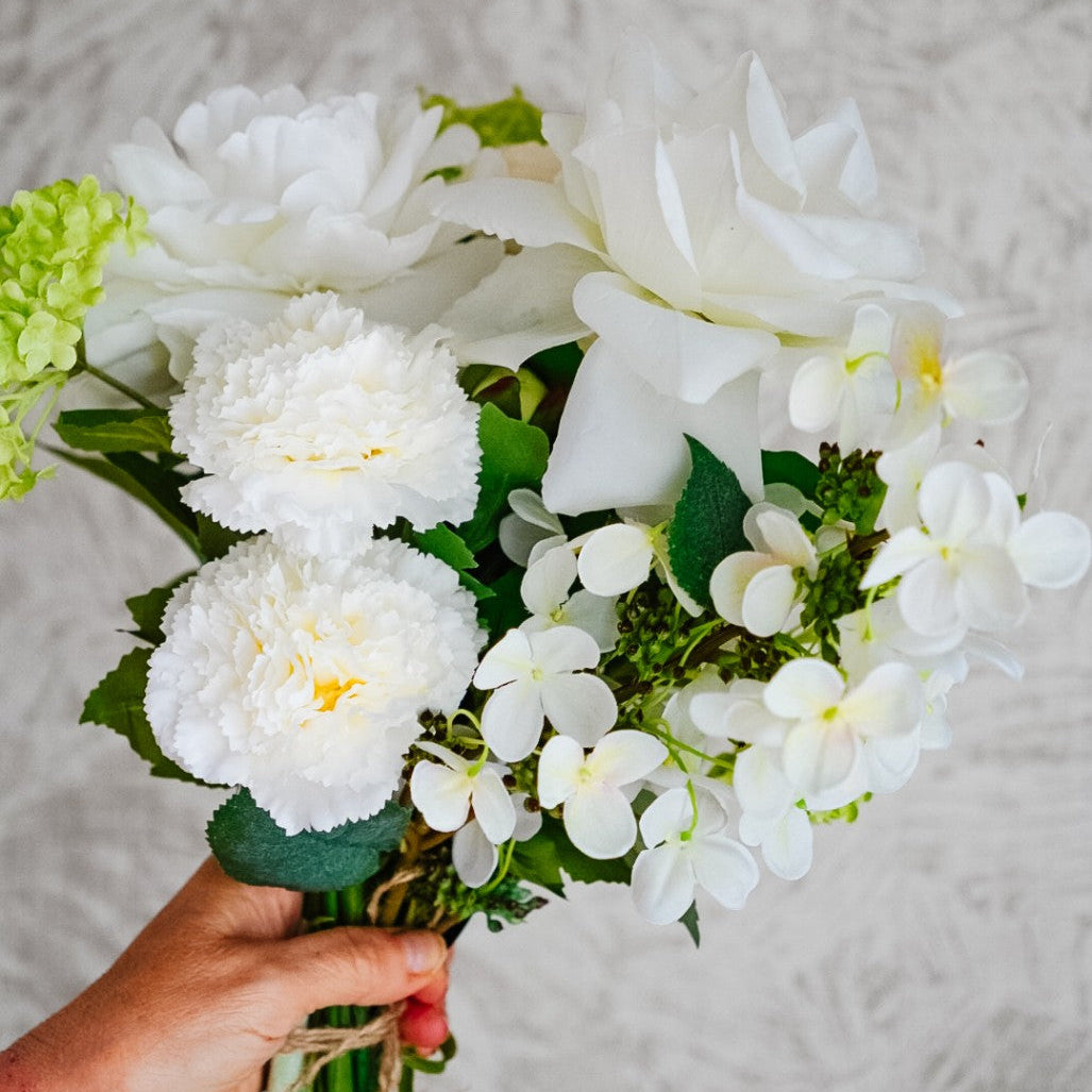 Alba silk flower bouquet held in hand, with white blooms and green foliage