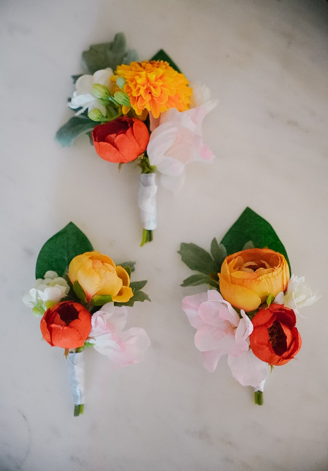 Silk flower buttonholes in orange, red and pink tones
