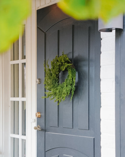 Small green 40 cm silk evergreen wreath on a grey entrance door