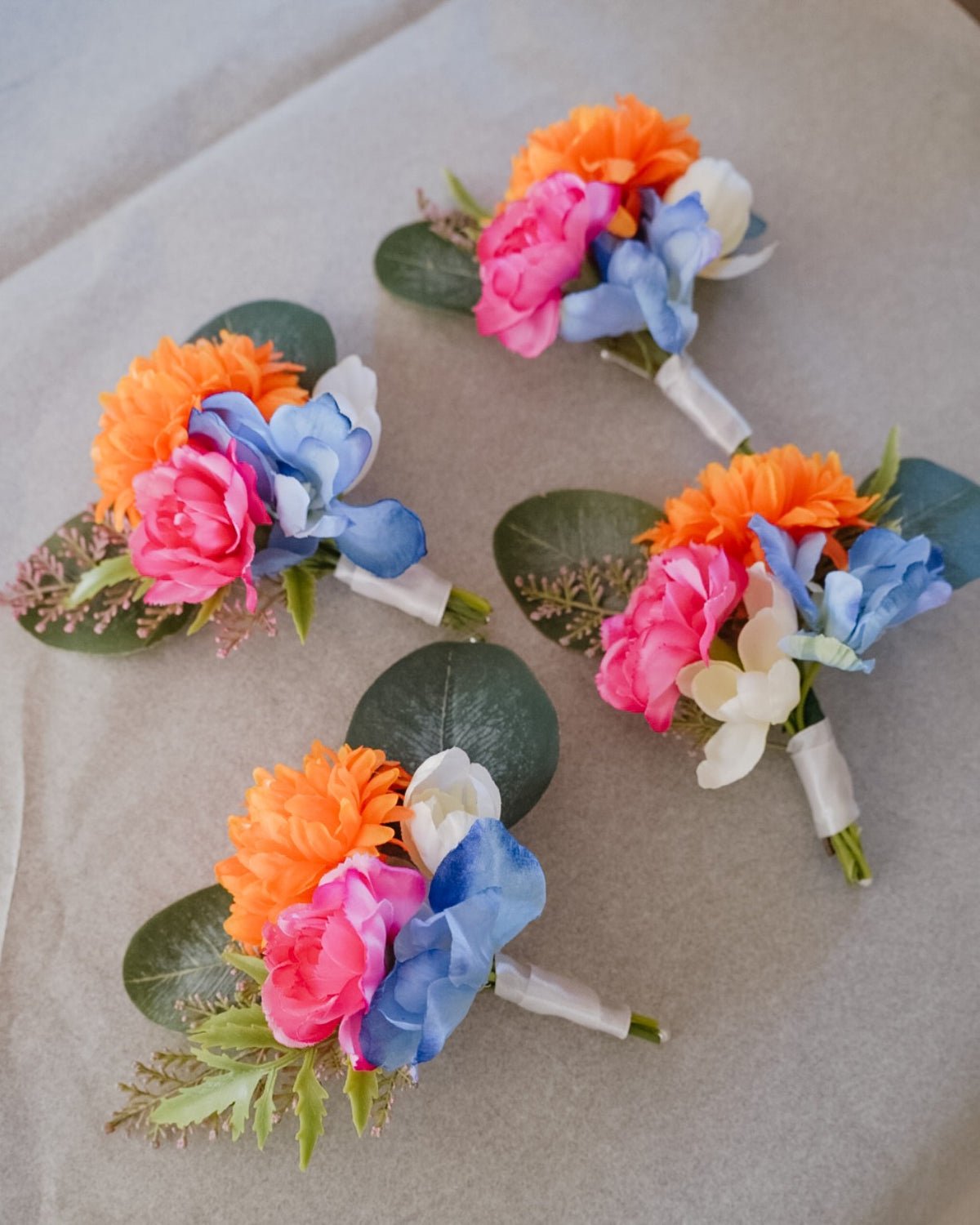 Colourful silk flower buttonholes in orange, pink and blue